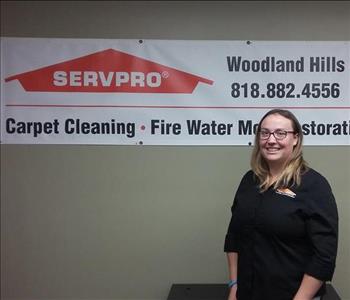 photo of female employee wearing glasses and standing in front of a SERVPRO sign